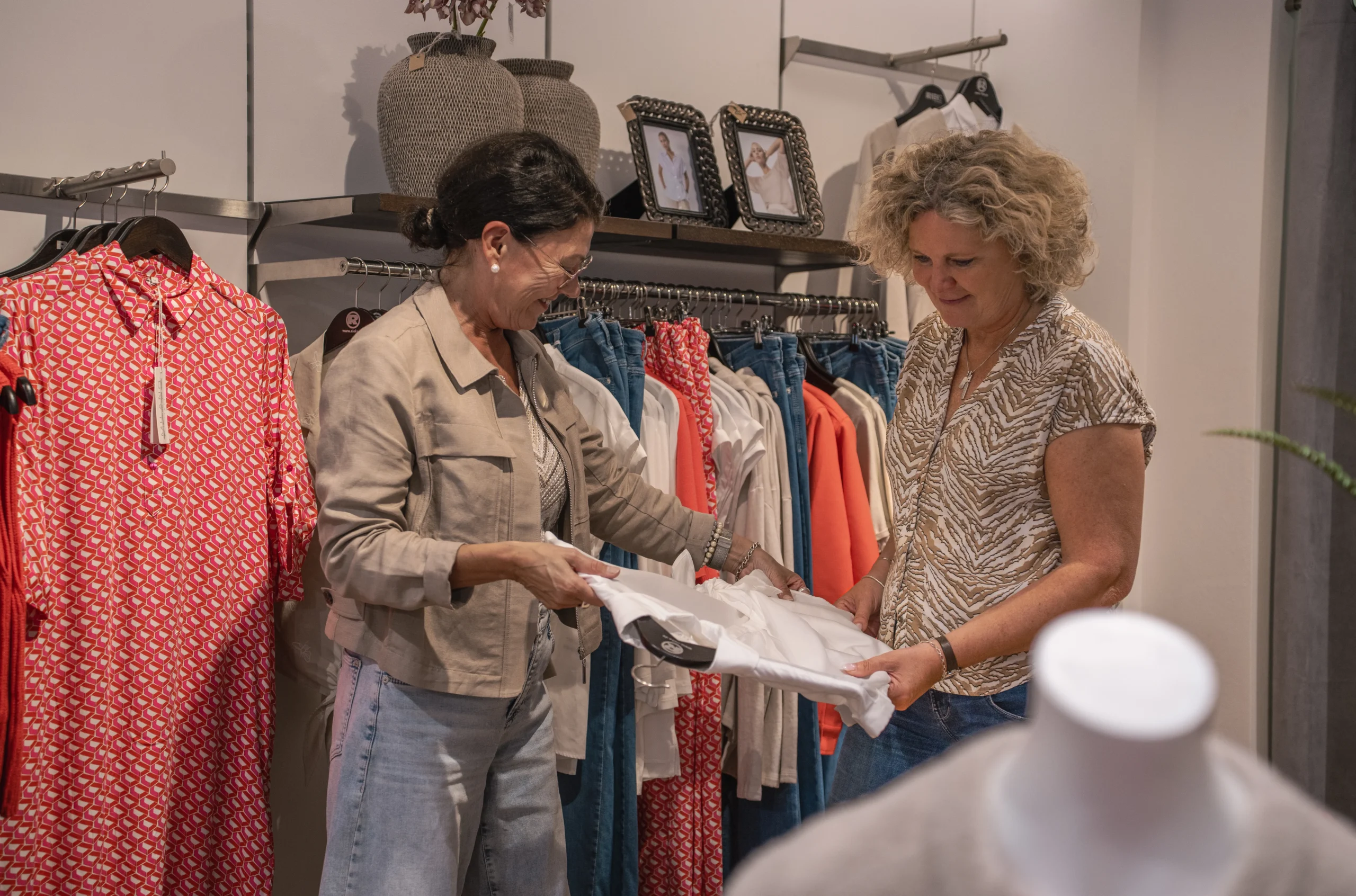 Zwei Frauen lachen gemeinsam beim Anprobieren von Kleidung im Modehaus Rieke